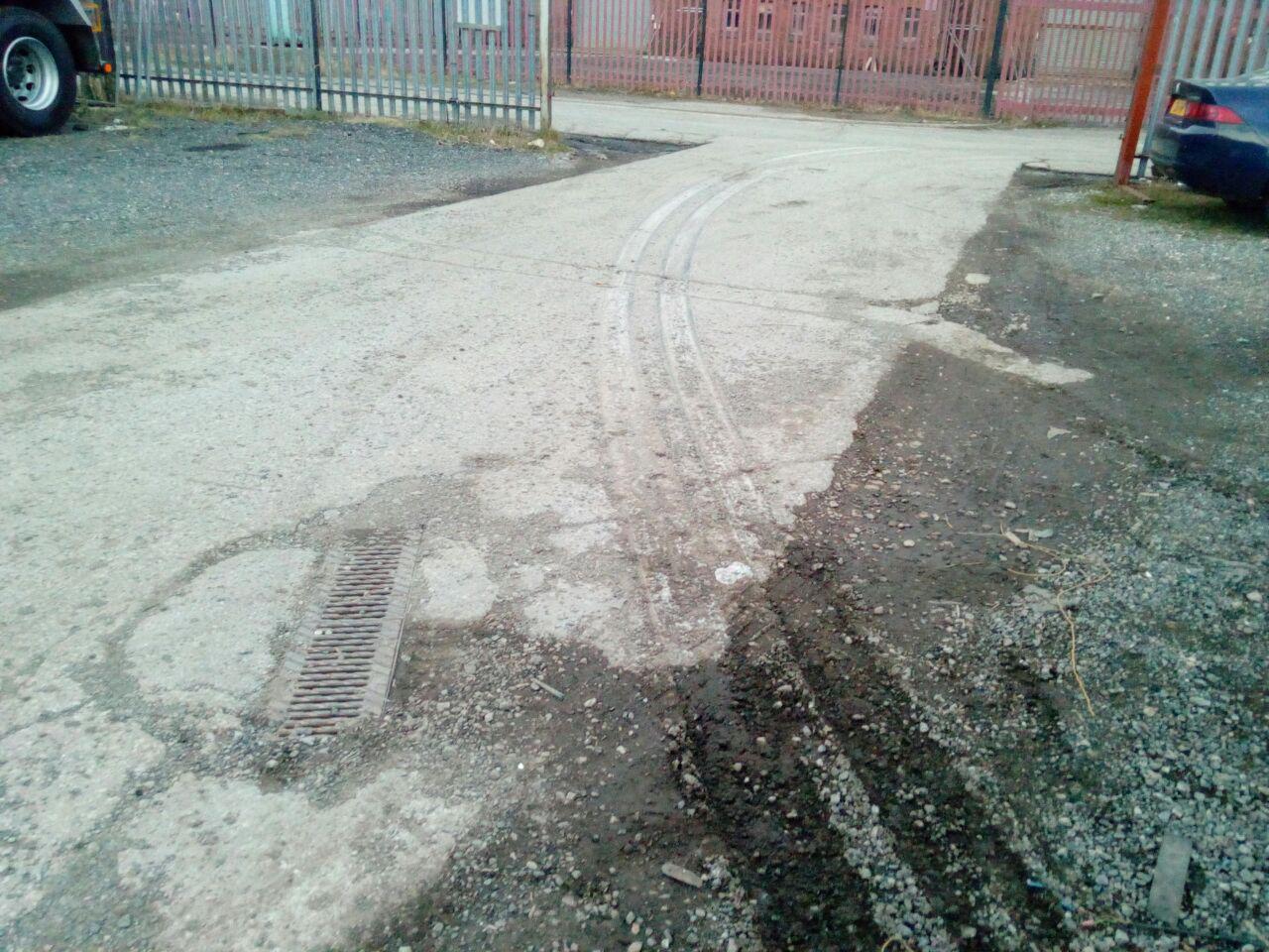A photograph looking back in the other direction, away from the
truck; showing the deep muddy tyre tracks transition to rubber and
gravel scrape marks on the concrete