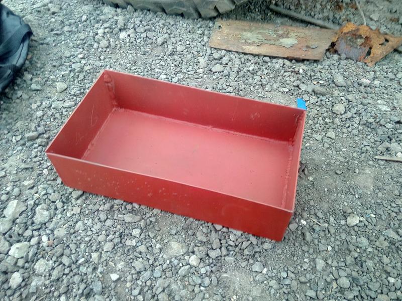 a red-painted welded steel tray -- just a box with no top --
sitting on a gravel floor.