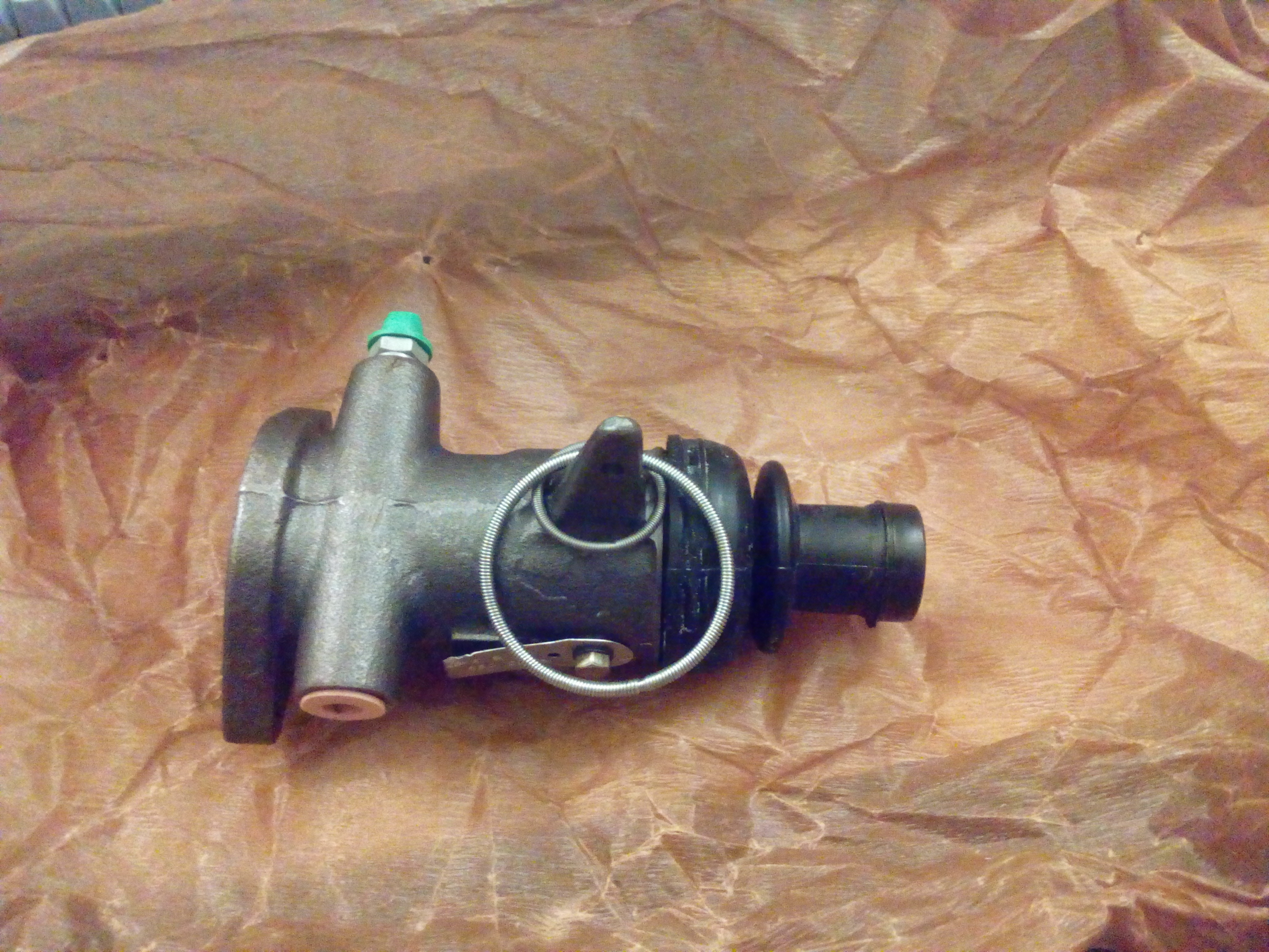 A transverse brake cylinder laying on unwrapped waxed
anti-corrosion paper. There are two spring retainers hanging off a
protrusion, that are meant to retain the rubber boot on the back.