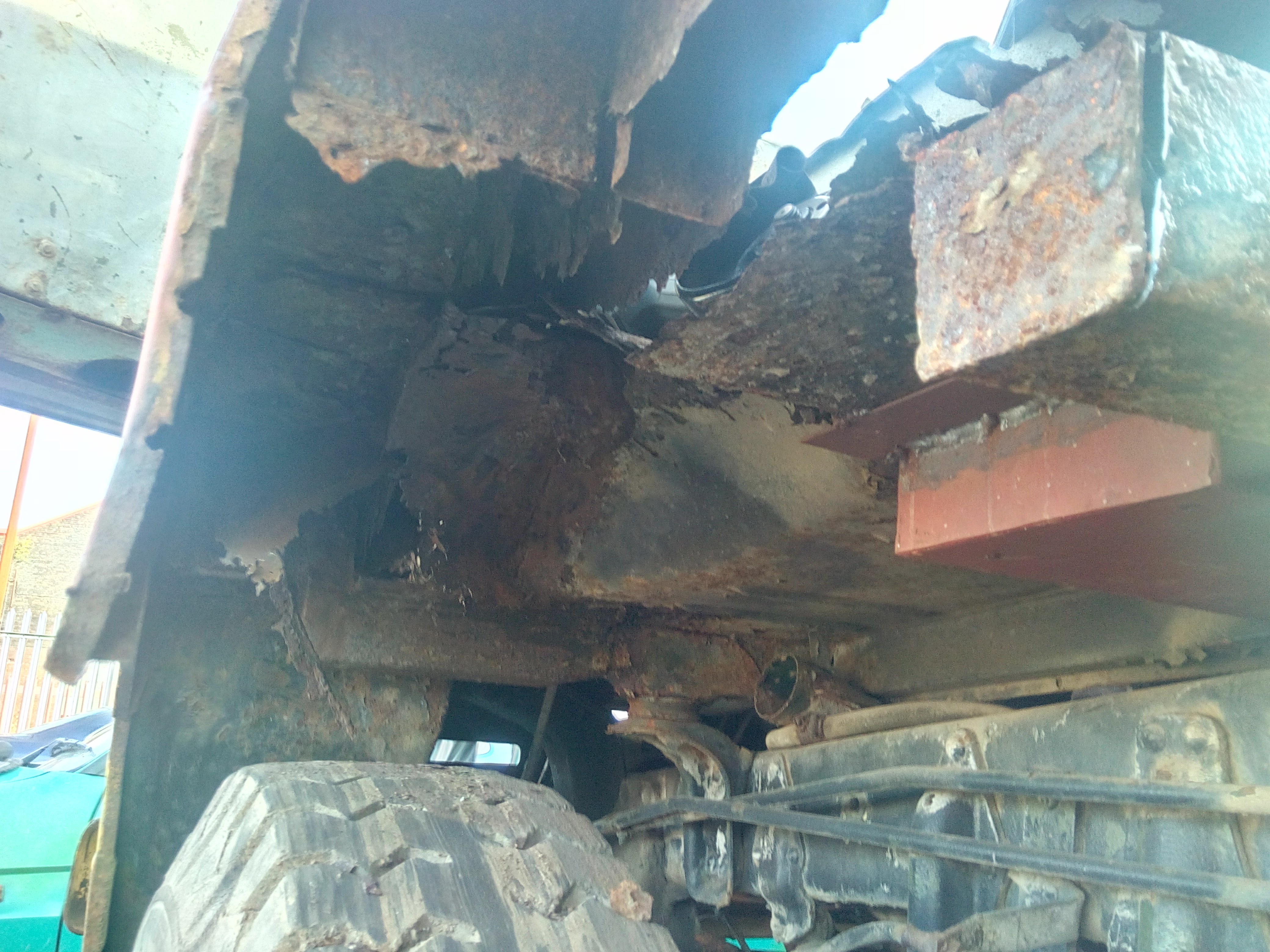 A photograph looking up underneath the passenger's side front
wheel well, showing ragged rotten metal everywhere you look. Large
patches of daylight are visible straight through the truck.