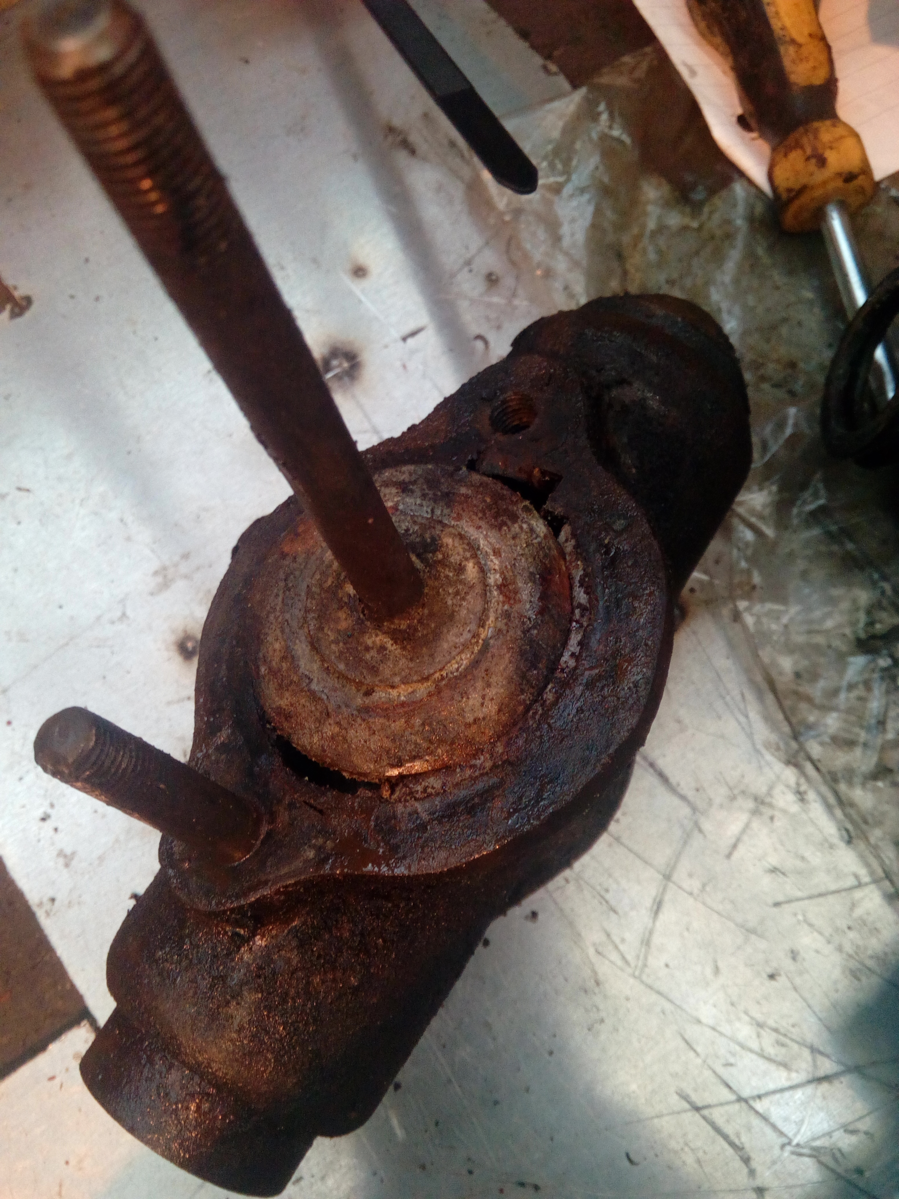 A lump of rusty metal sitting on a workbench, there are two studs sticking out of it, and a hole where a third should be. The central</p>
<a class=