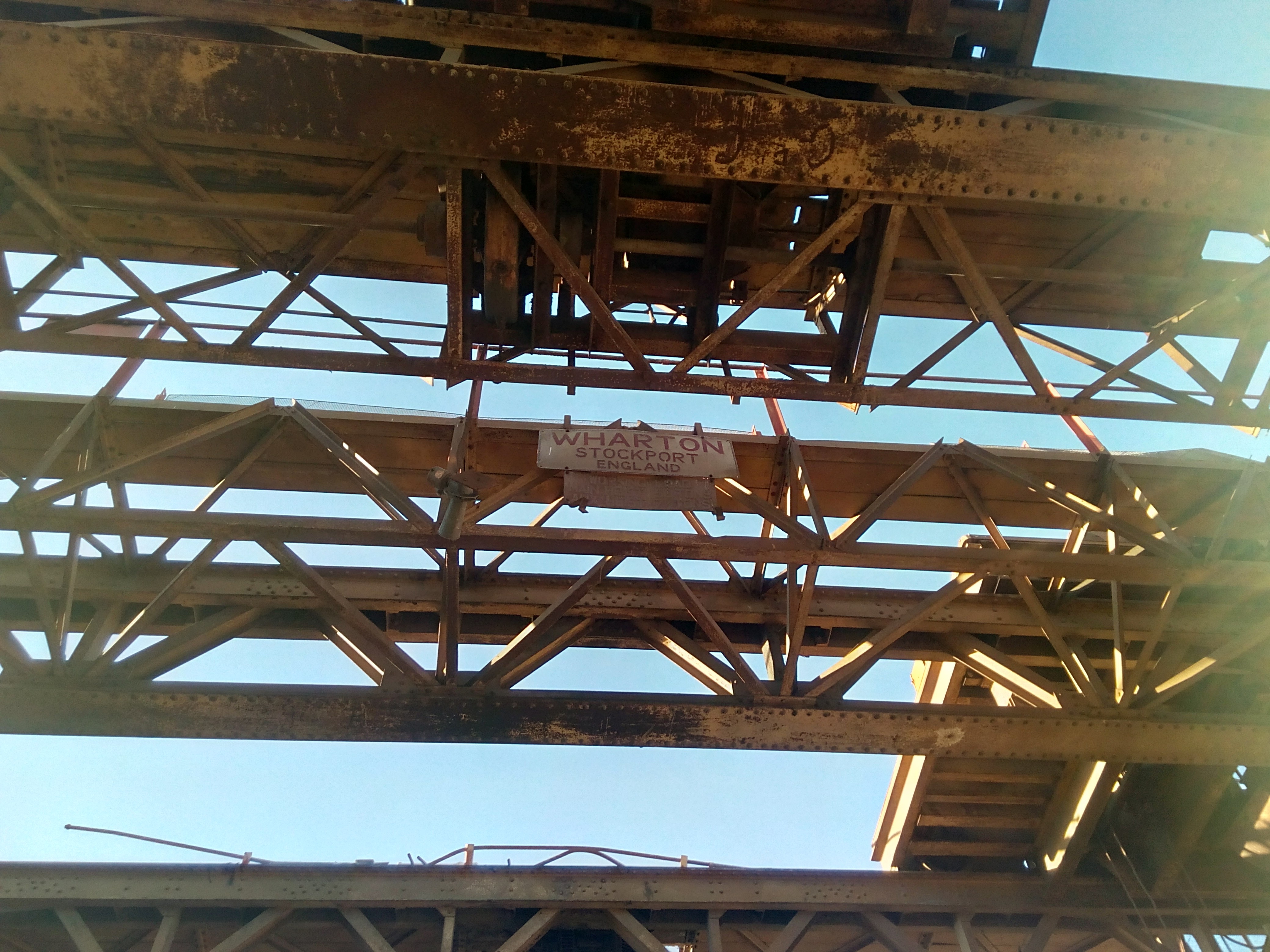 Photograph taken looking up at the underside of a pair of very
large overhead cranes. A large manufacturers' plate, reading 'Wharton,
Stockport, England' is visible; below that is a very faded rating
plate, reading 'Working Load, main hoist, Fifty tons. Aux hoist: Seven
and a half tons.