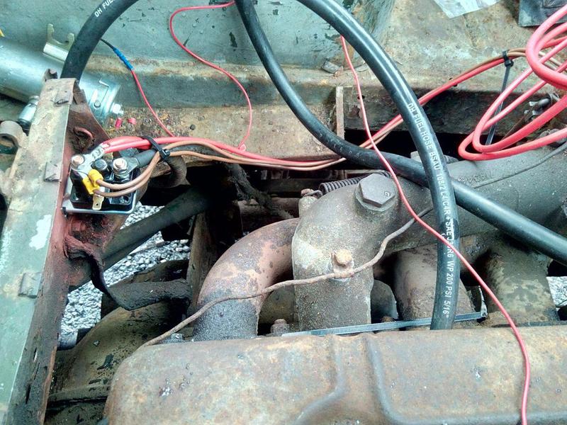 A photograph of a very rusty truck engine and cab floor, with
some messy wiring hastily added to a new starter solenoid bolted to
some sheet metal.