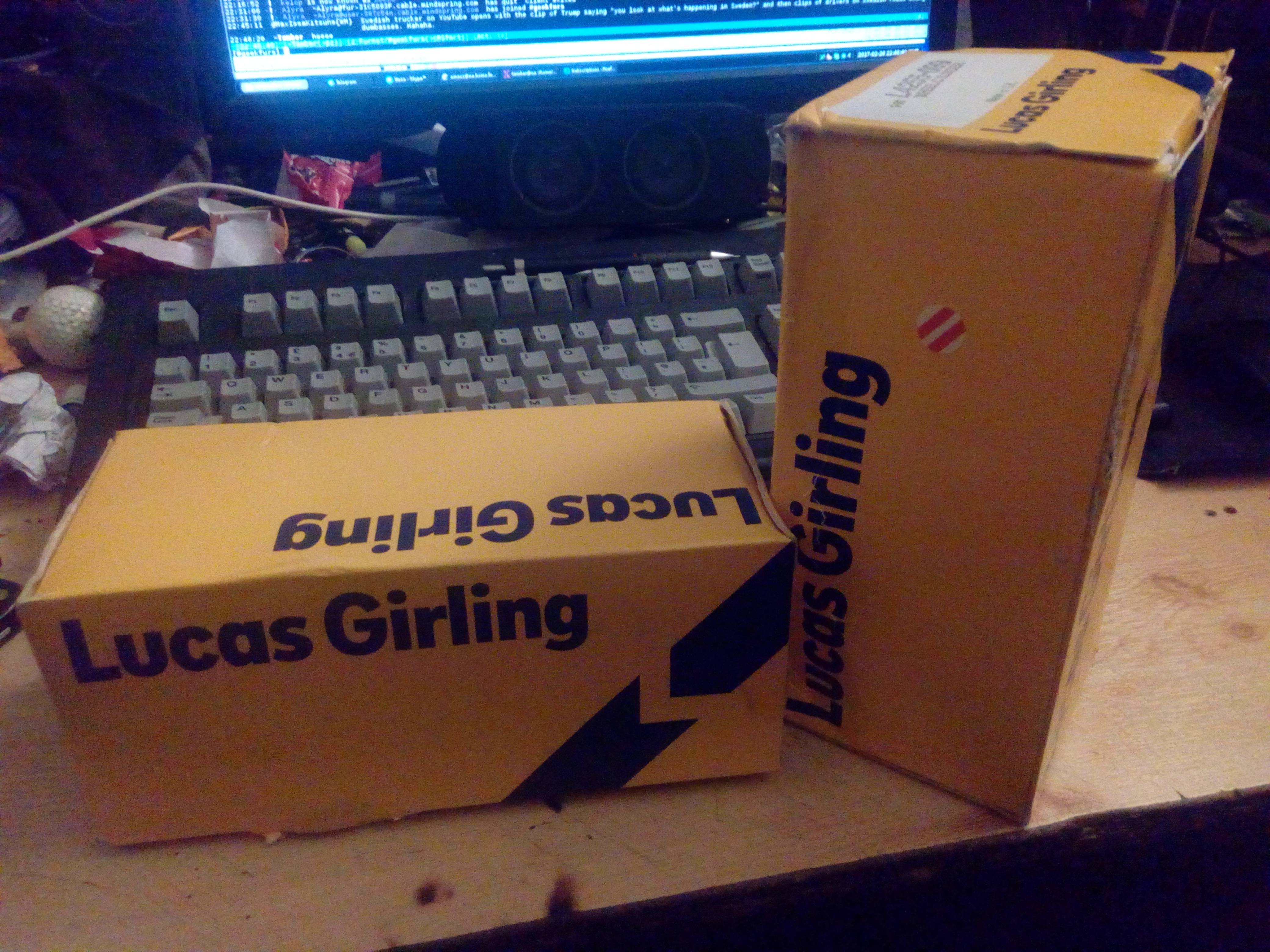 Photograph of a desk, with two yellow cardboard boxes sat on
it. The boxes are labelled, in dark blue text, 'Lucas Girling'.