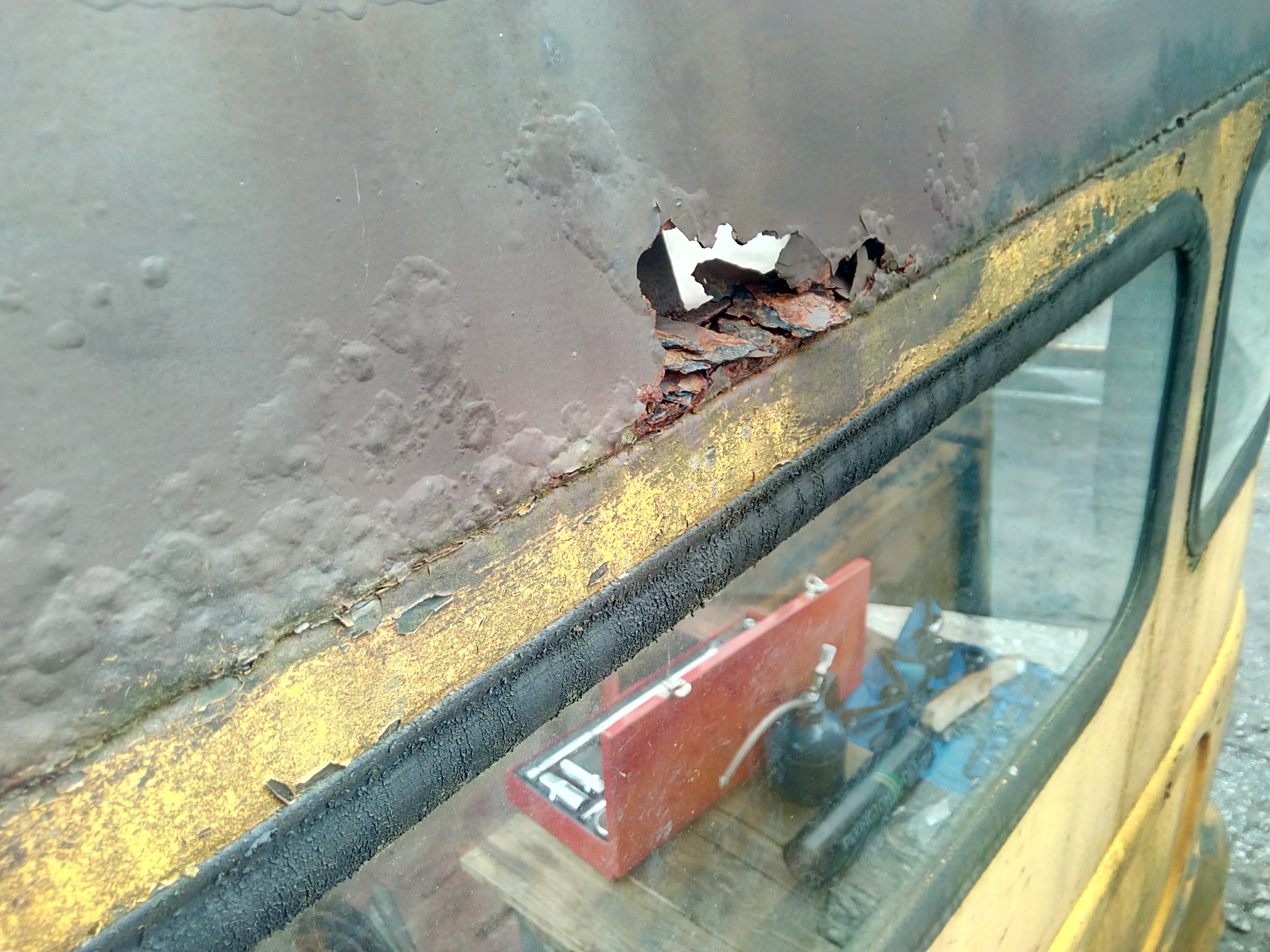 Photo of the back of the cab roof, where a crusty rust-hole has
been pushed through at a panel edge. There are also further bubbles
underneath the paint indicating additional rust.