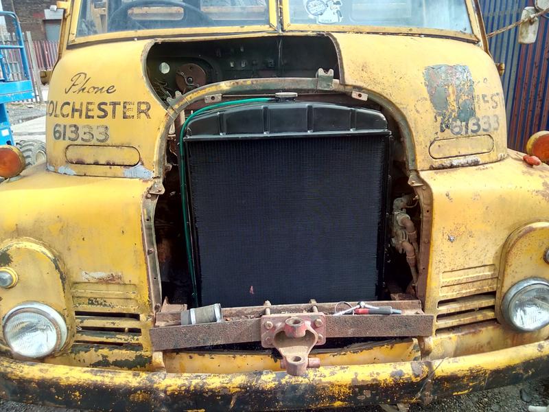 A yellow Bedford RL, with the radiator grille and upper cowl panels removed, exposing a very shiny black radiator that has a small copper-coloured scuff in the lower middle.