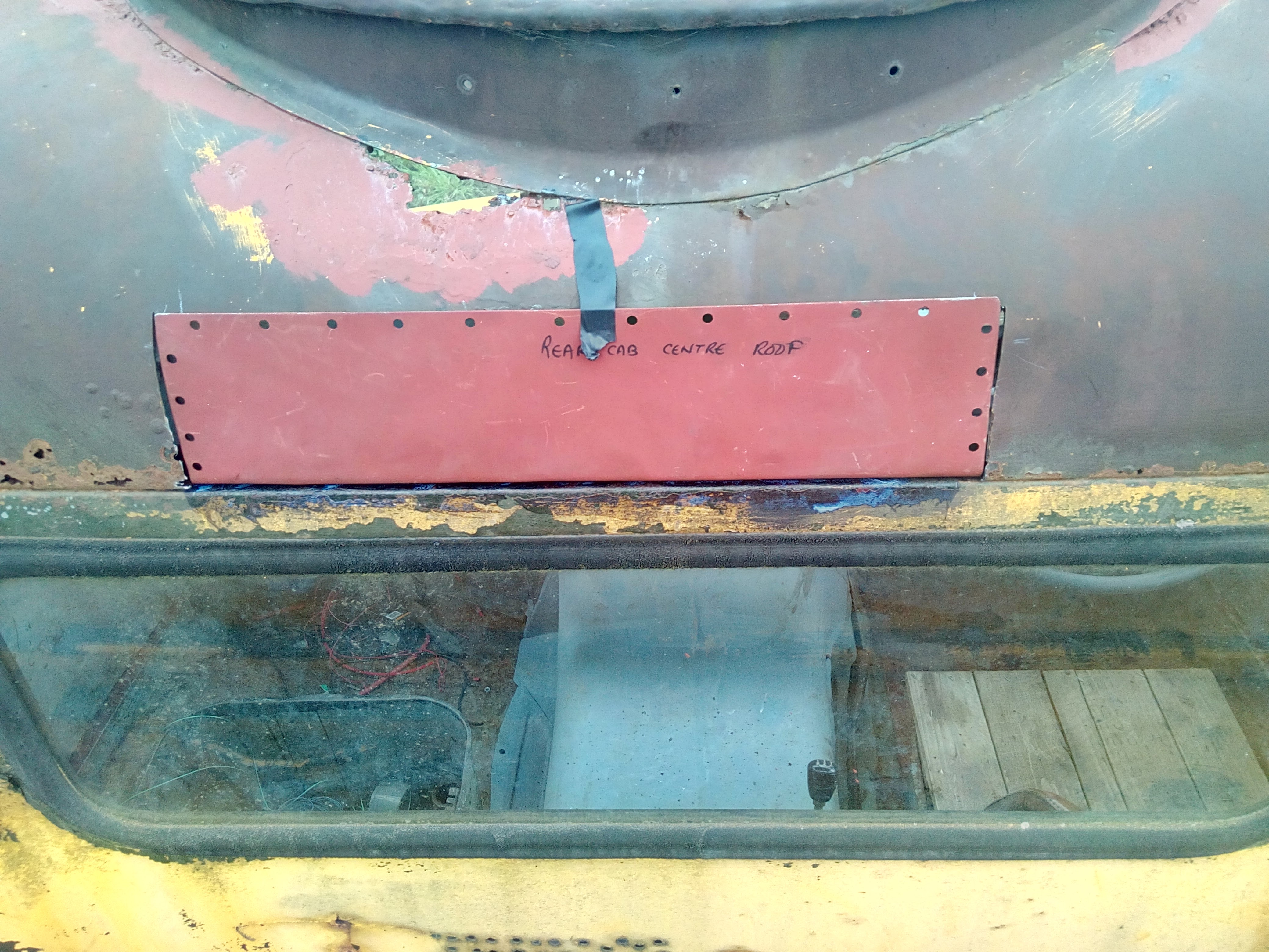 The back of the cab roof, now with the large hole filled by a
red-painted piece of metal that almost completely fills the hole. The
filler metal has a series of holes punched into it around the edges,
because I thought I was going to need them to weld to the existing
metal of the cab.
