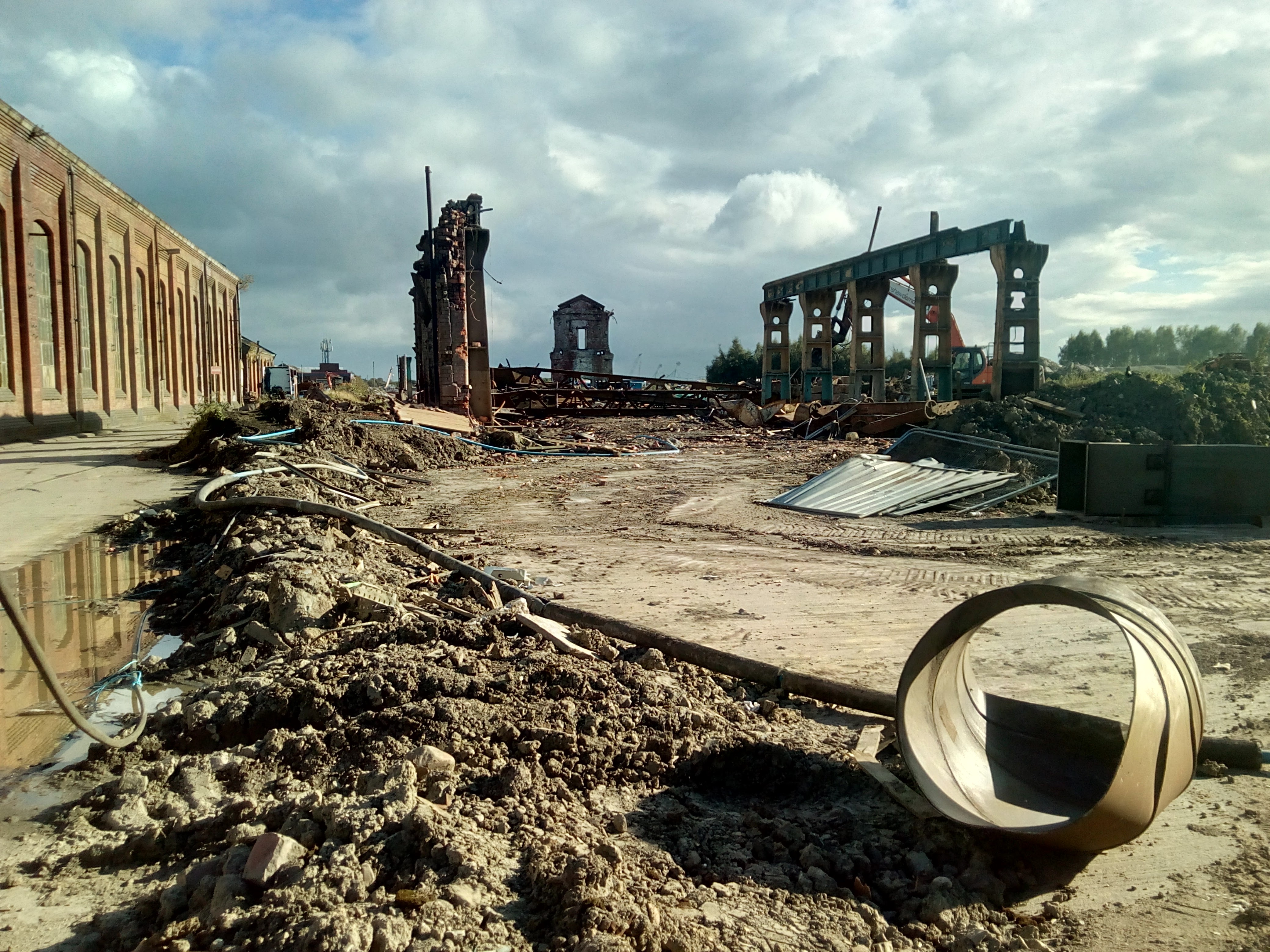 Photograph across the demolition site, along the section of
overhead-crane track. The cranes have been pushed off the end, and now
lie as a heap of twisted metal on the ground. In the distance, the
central pillar of the building looms over the wasteland.