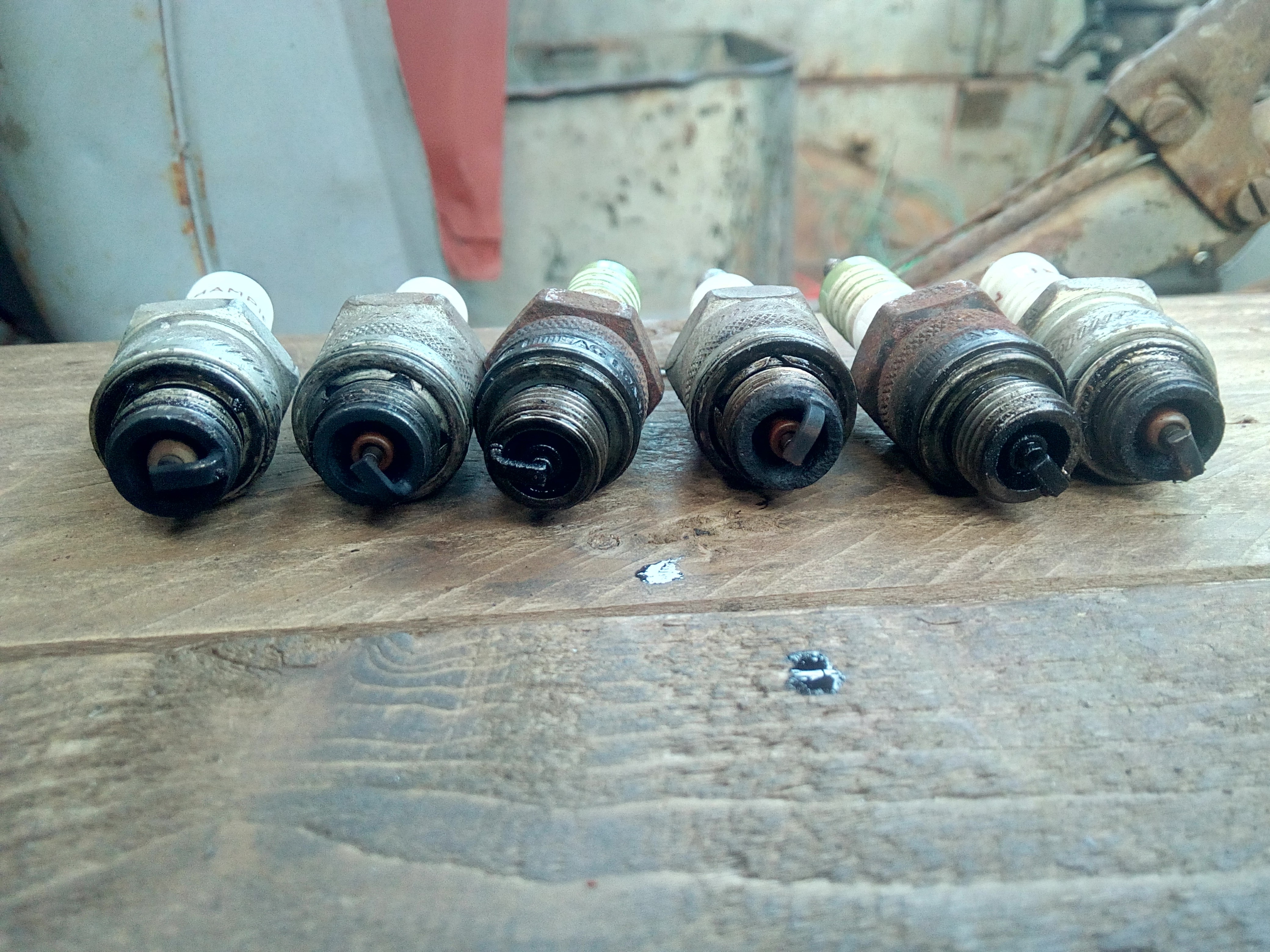 Old spark-plugs lined up along a wooden board. They are all dark
and oily.