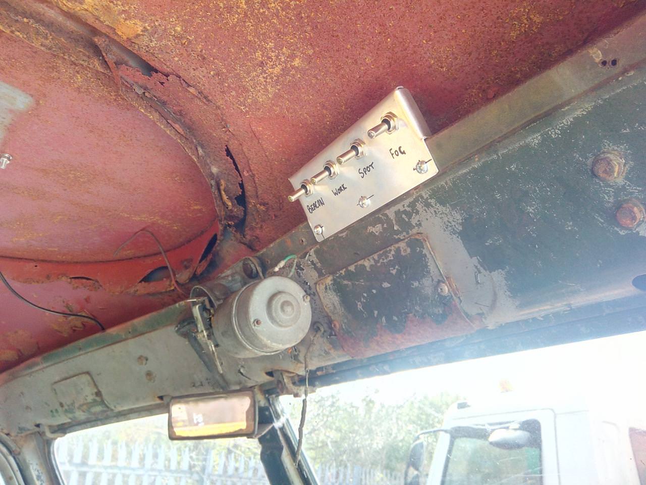 A shiny aluminium switch panel bolted to the truck's upper dash
panel. The panel has 4 switches in it, hand-labelled with sharpie:
Beacon, Work, Spot, and Fog.
