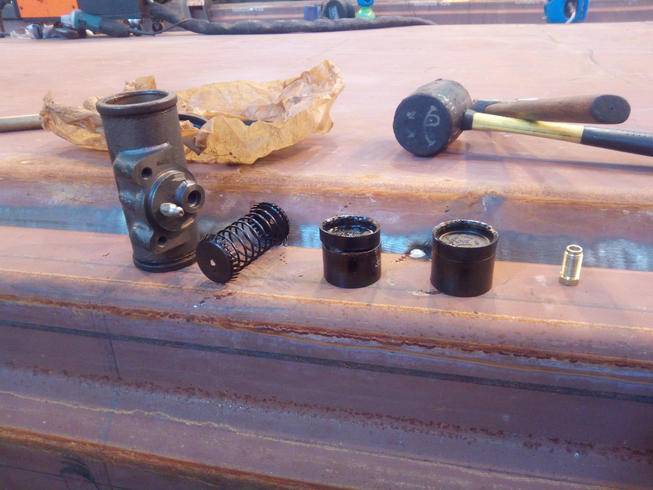 A front wheel cylinder disassembled on an upturned tipper truck
body, there is the outer body of the wheel cylinder, an expansion
spring and then the two seals and pistons that the brake fluid
operates on. One of the cup seals is sitting up at a funny angle.