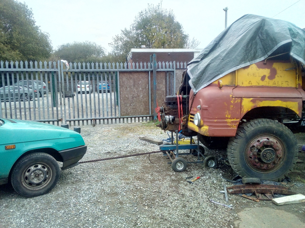 The engine on its cradle is starting to be inched out of the
front of the truck, towed on a piece of rope by a tatty green car.