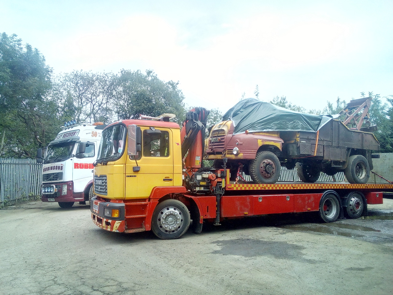 "Bedford chained down on the back of an MAN slide-bed recovery truck, with a Volvo FH wrecker waiting in the background"