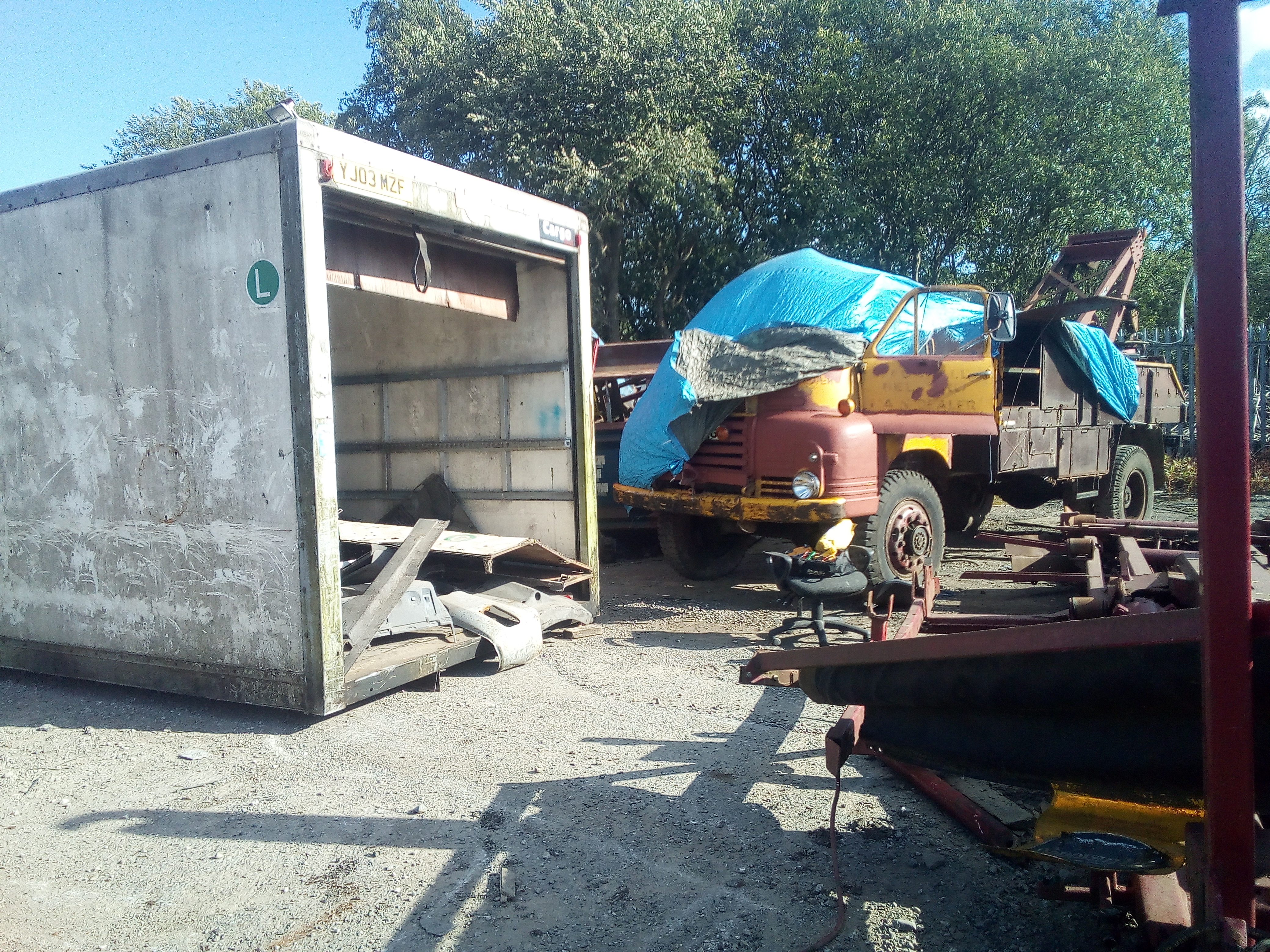The Bedford boxed in by scrap on all sides. A scrap-filled dump
truck body to the right, a scrap hookloader equipment to the left, and
a box-truck body dumped in front of it.