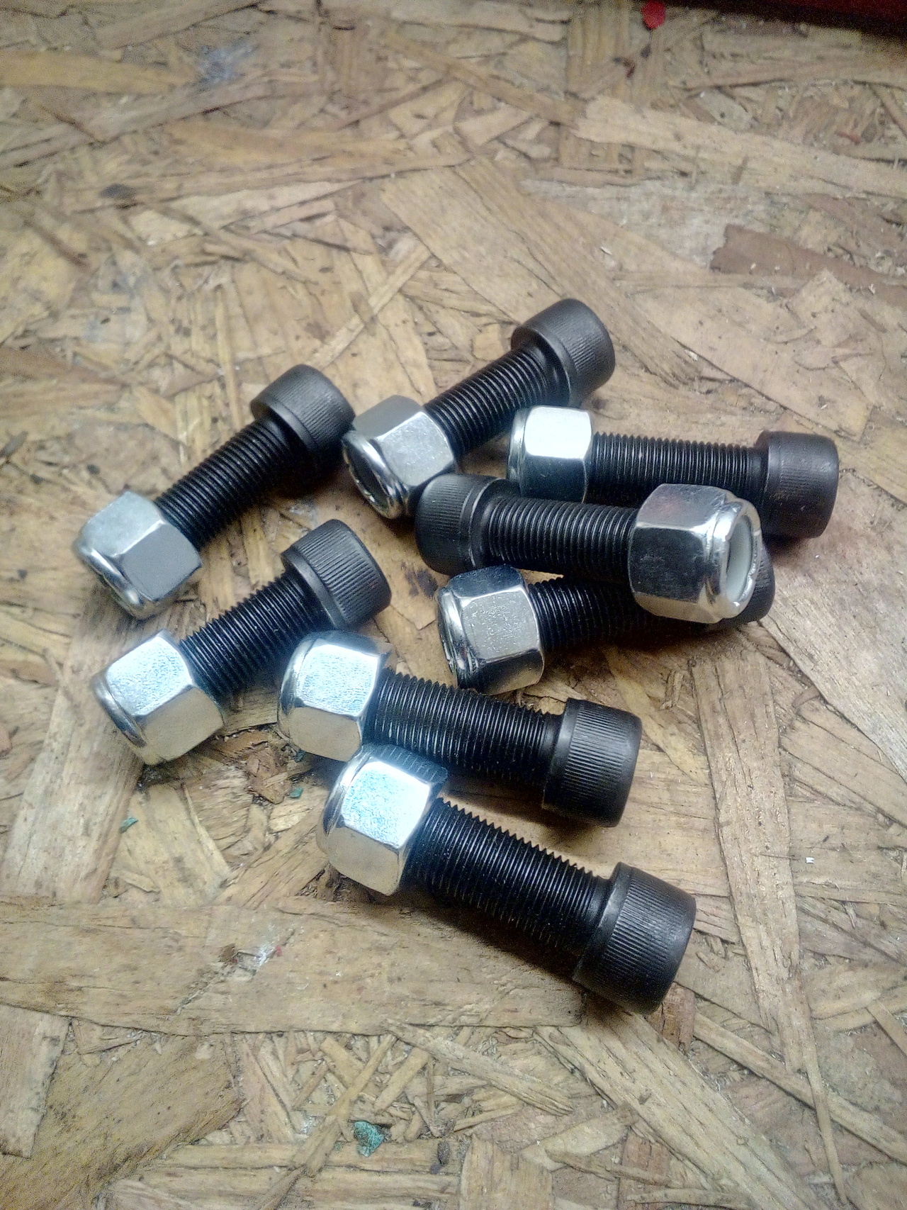 8 cap-head bolts and nyloc nuts, laying on a rough wooden bench.