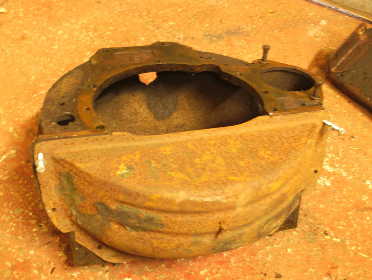 The flywheel housing on the workshop floor, tilted onto its back,
now with the stamped steel lower cover fitted, that closes in the
gaping hole for the removal of the flywheel.
