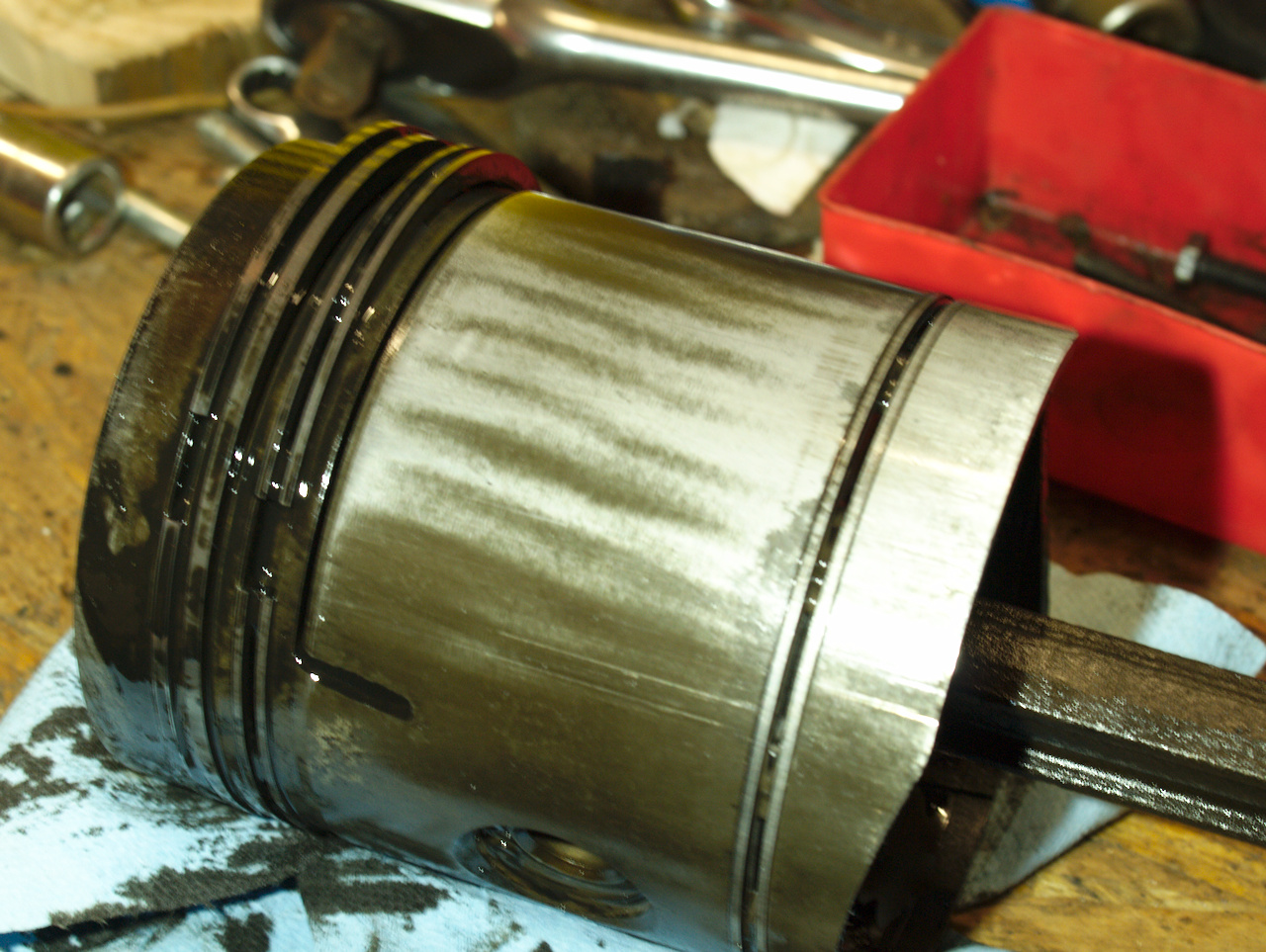 A piston laying on a workbench, showing machining marks that put
a slot into the skirt of the piston just below the compression
rings. The rest of the piston skirt is solid.