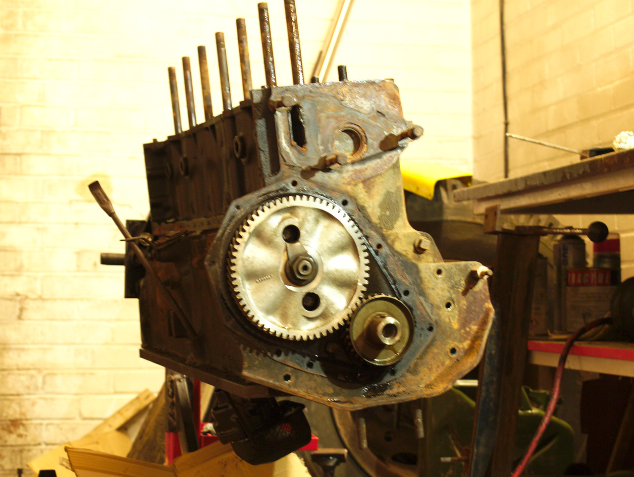 The partially-stripped engine on the stand, with the timing cover
removed and exposing the timing gears; with a large aluminium cam gear
meshed with the smaller crank gear.