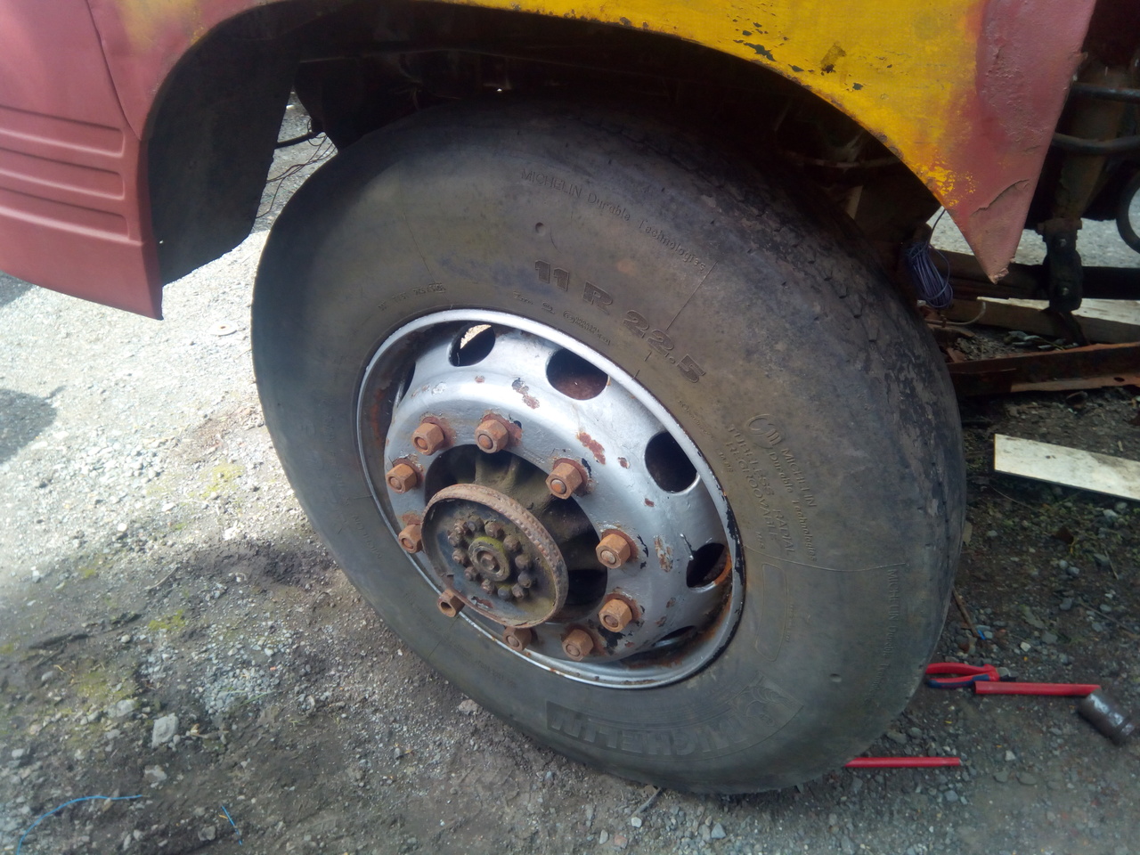A flakey silver modern truck wheel partially bolted up to the
Bedford's front axle.